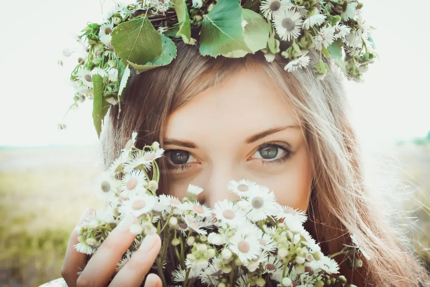Portrait d'une femme au visage partiellement caché par des pâquerettes, coiffée d'une couronne de fleurs et de feuillage